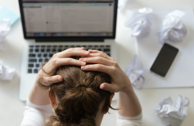 retrato de mulher agarrando a cabeça na mesa perto do notebook aparentemente com burnout