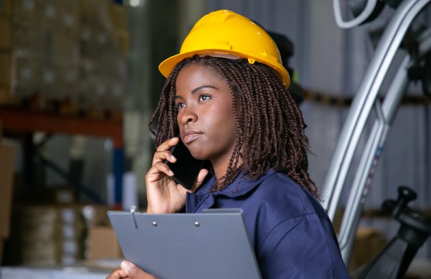Engenheira-negra-de-capacete-de-seguranca-em-pe-no-armazem-e-alando-ao-celular.